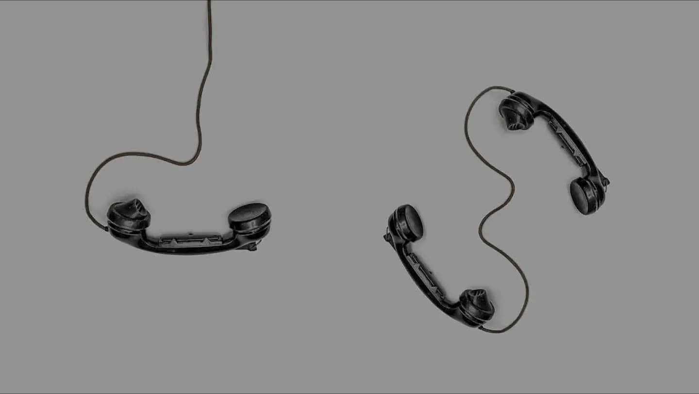 Two black vintage rotary phone handsets with cords are shown on a plain gray background. One handset is on the left and the other is on the right.