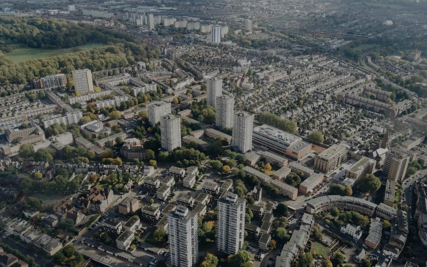 Aerial view of a dense residential neighborhood in a city. The neighborhood has a mix of tall apartment buildings and tree-lined streets.